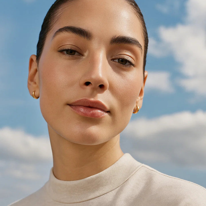 Woman wearing a beige top against a blue sky with clouds